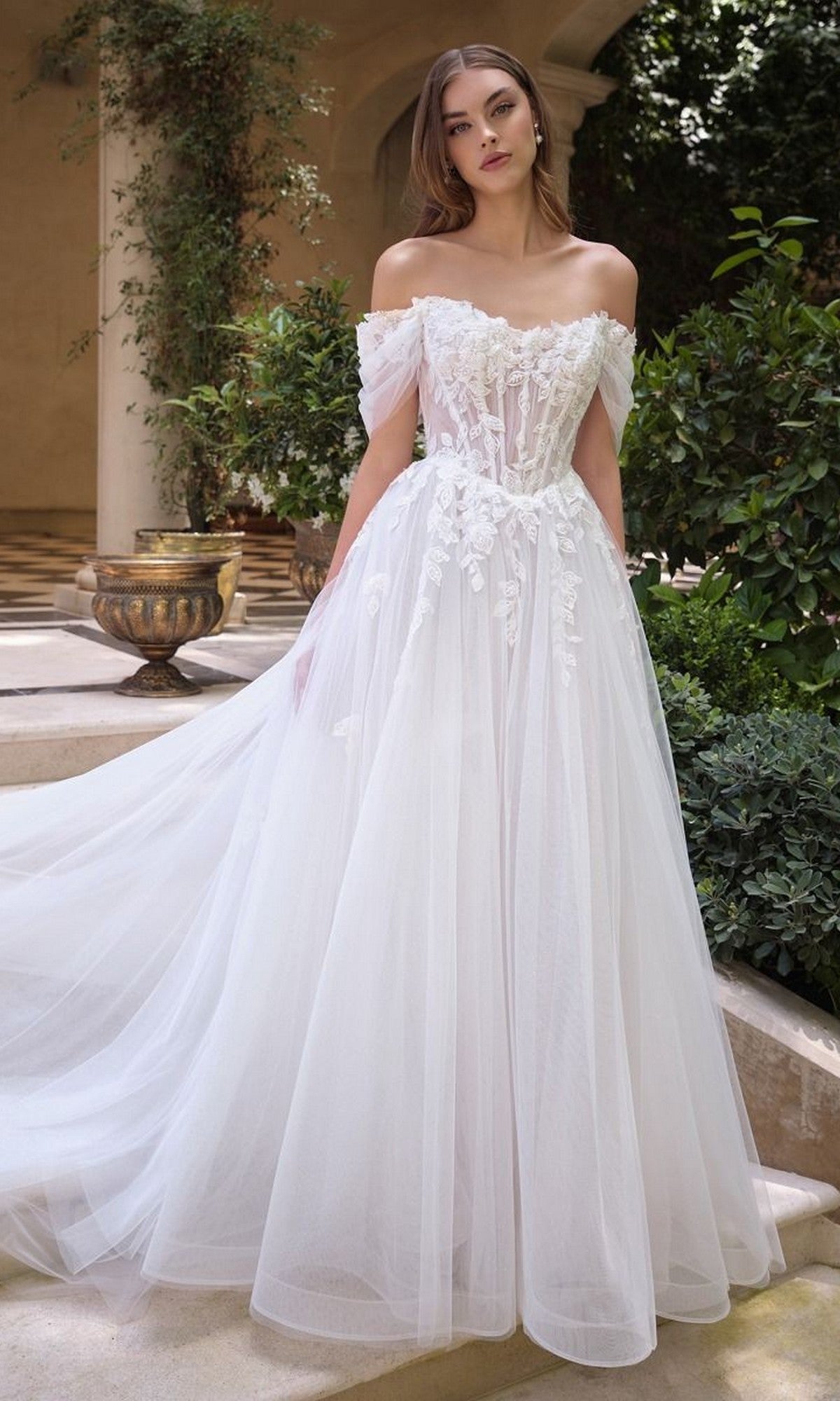 A woman stands outdoors in the Andrea and Leo WL089 long wedding dress, featuring off-the-shoulder floral lace appliques and a voluminous A-line tulle skirt for a romantic, elegant bridal look.